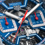 Close-up of a TAG Heuer Monaco Chronograph watch face with a skeletonized dial, blue subdials, white hour and minute hands, red second hand, and visible Heuer 02 mechanical movement.