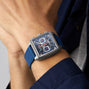 Someone is wearing a TAG Heuer Monaco Chronograph with a square face, blue strap, and skeletonised dial on their wrist.