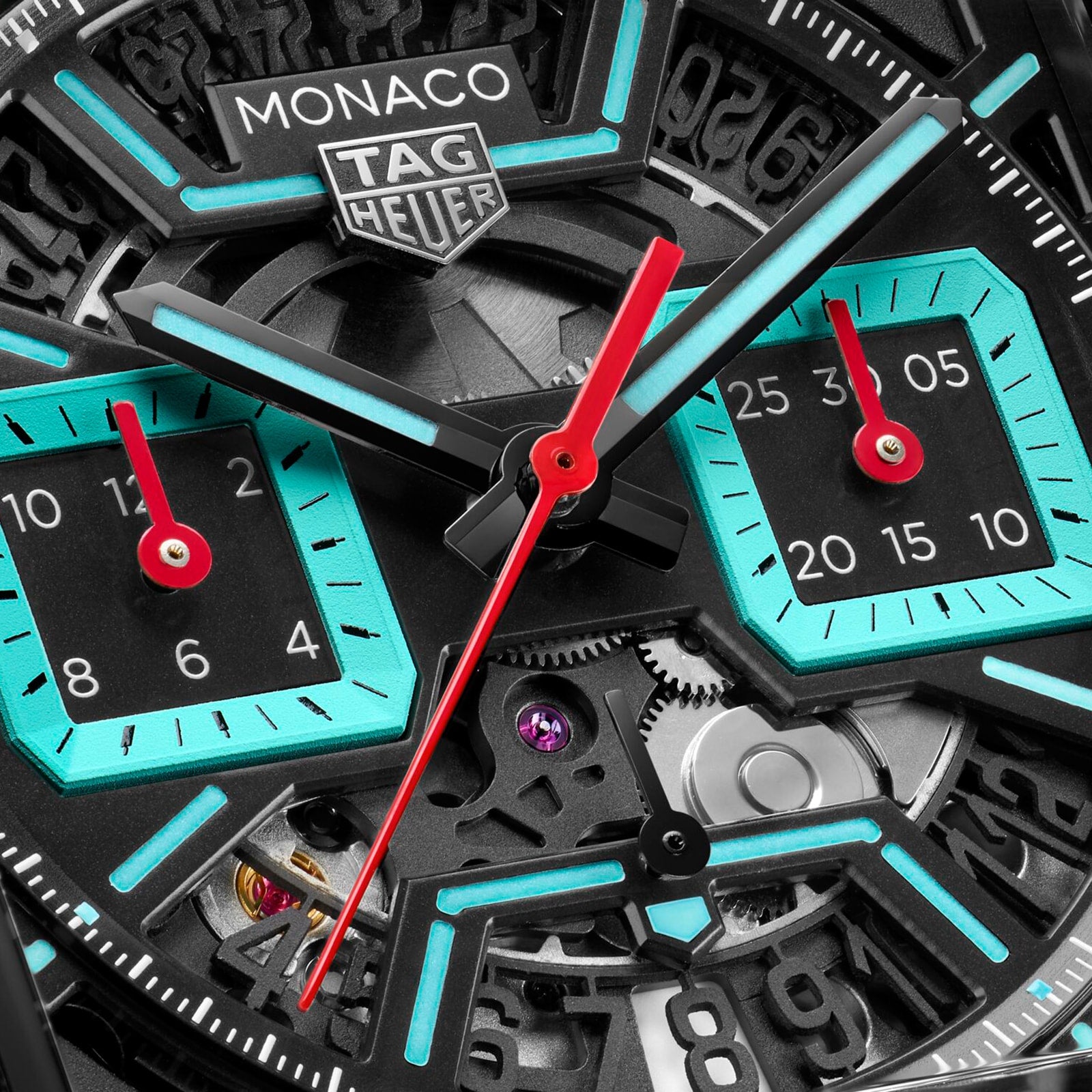 Close-up of a TAG Heuer Monaco Chronograph watch face, featuring red hands, turquoise accents, and visible gears.
