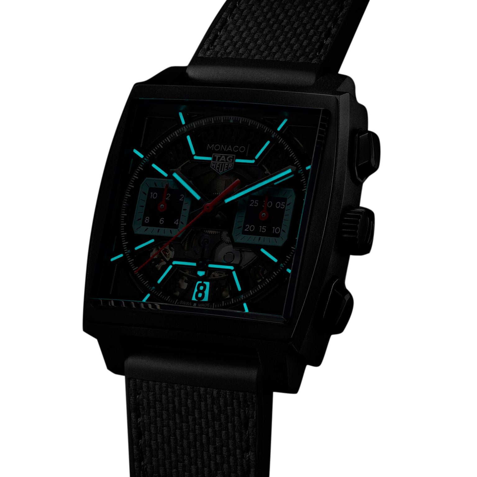 The TAG Heuer Monaco Chronograph features a black square face, luminous markers and hands, titanium case, and black textured strap, shown against a white background.