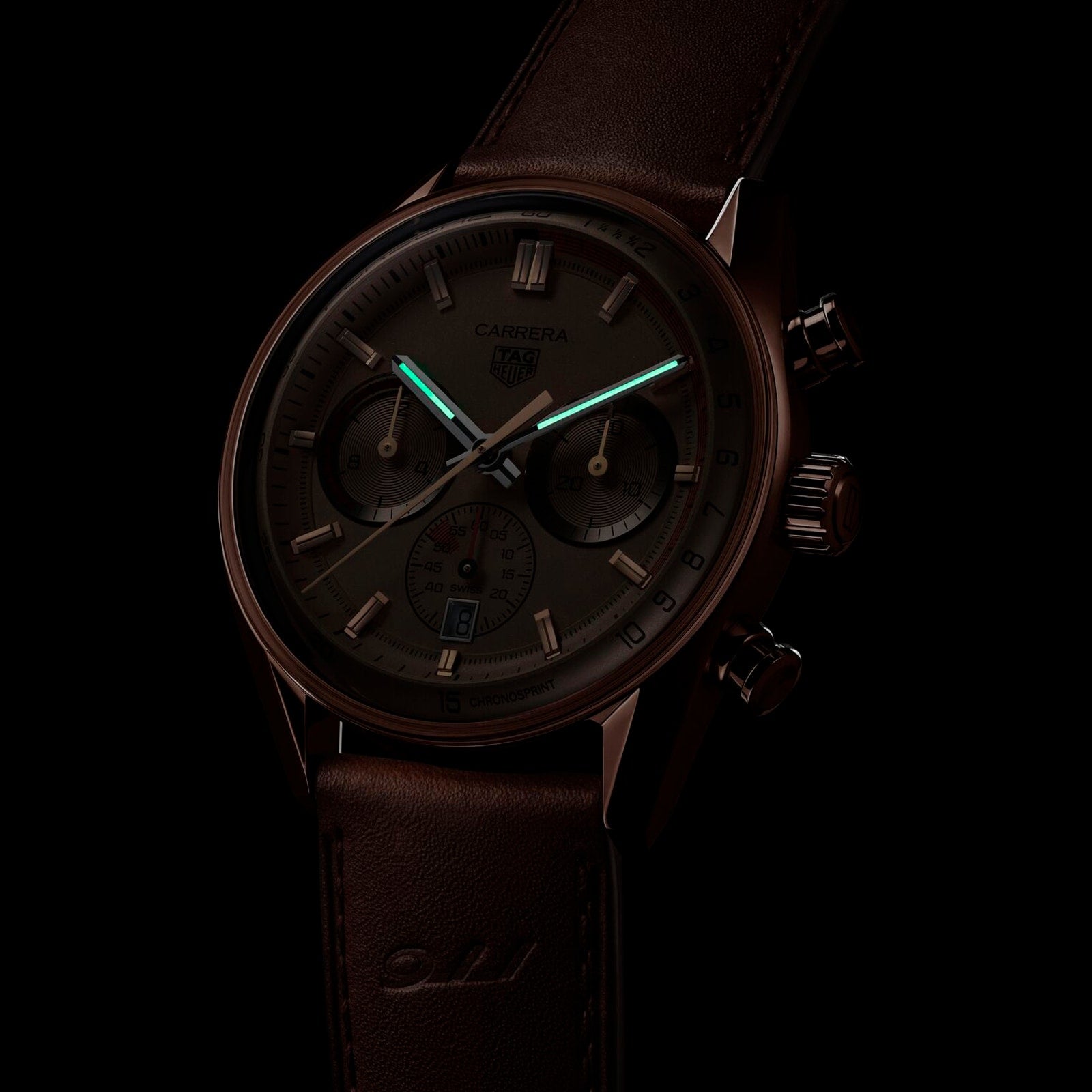 A dark-toned image of the TAG Heuer Special Edition Carrera Chronosprint x Porsche shows its leather strap and chronograph hands, powered by an automatic movement, partially illuminated with a green glow.