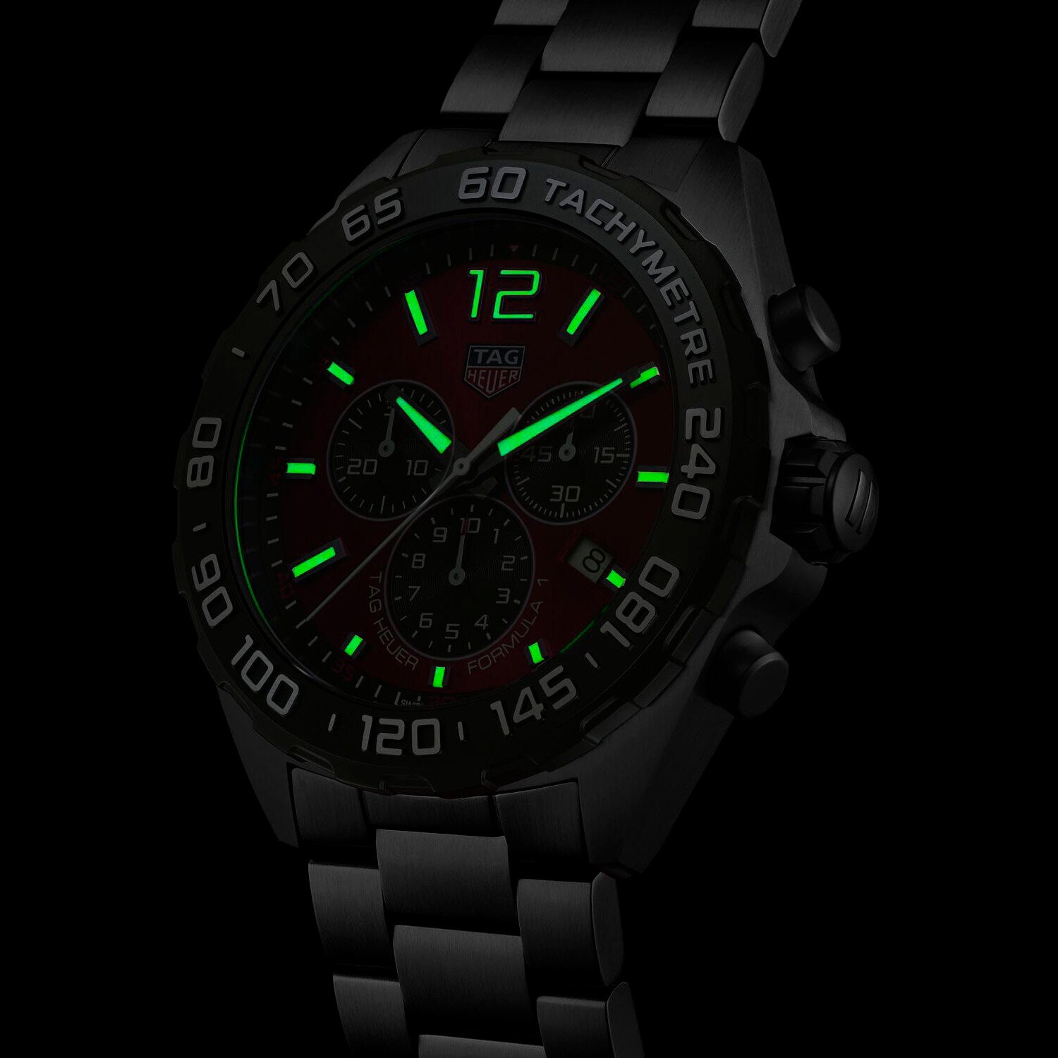 A TAG Heuer Formula 1 Chronograph wristwatch with luminescent green markers, hands, and indices glows in low light.