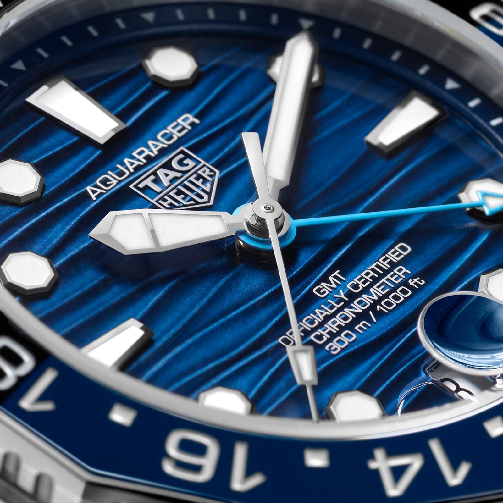 Close-up of a TAG Heuer Aquaracer Professional 300 GMT watch face with blue textured dial, white hour markers, date window, and silver hands, showcasing precision and durability with 300 m/1000 ft water resistance.