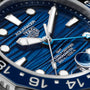 Close-up of a TAG Heuer Aquaracer Professional 300 GMT watch face featuring a blue textured dial, silver markers and hands, and white text detailing the model and water resistance.