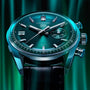 A close-up of the TAG Heuer Carrera Chronograph wristwatch, featuring a teal dial, date window, and chronograph on a black leather strap with metallic casing, set against a green background.