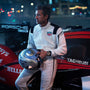 A man in a white racing suit stands by a Porsche race car at night, holding a helmet and wearing the TAG Heuer Limited Edition Carrera Chronograph x Porsche 963 watch.
