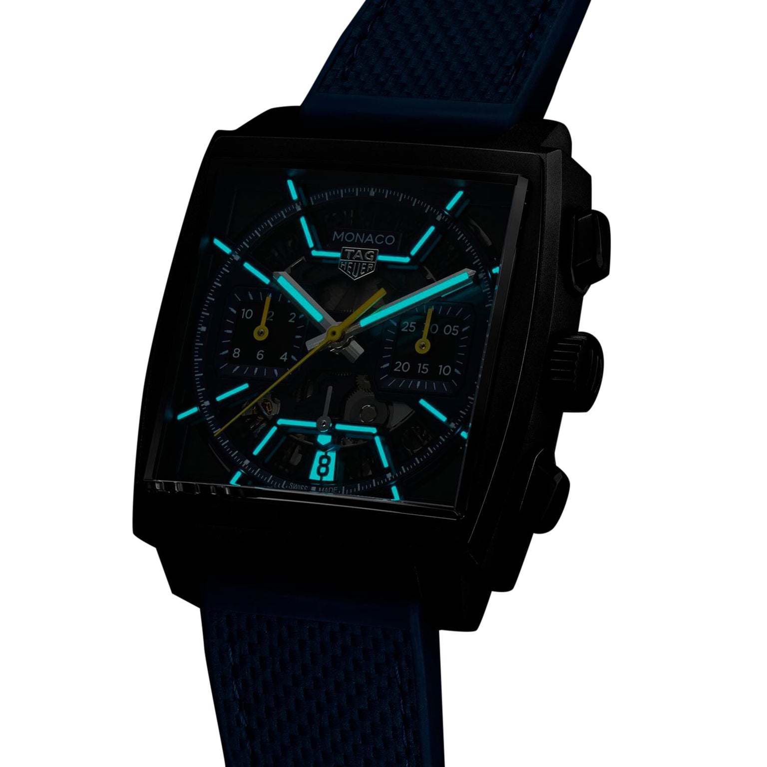 A TAG Heuer Monaco Chronograph watch with a square case, luminous blue markers and hands, black casing, and a textured blue strap is displayed against a white background.