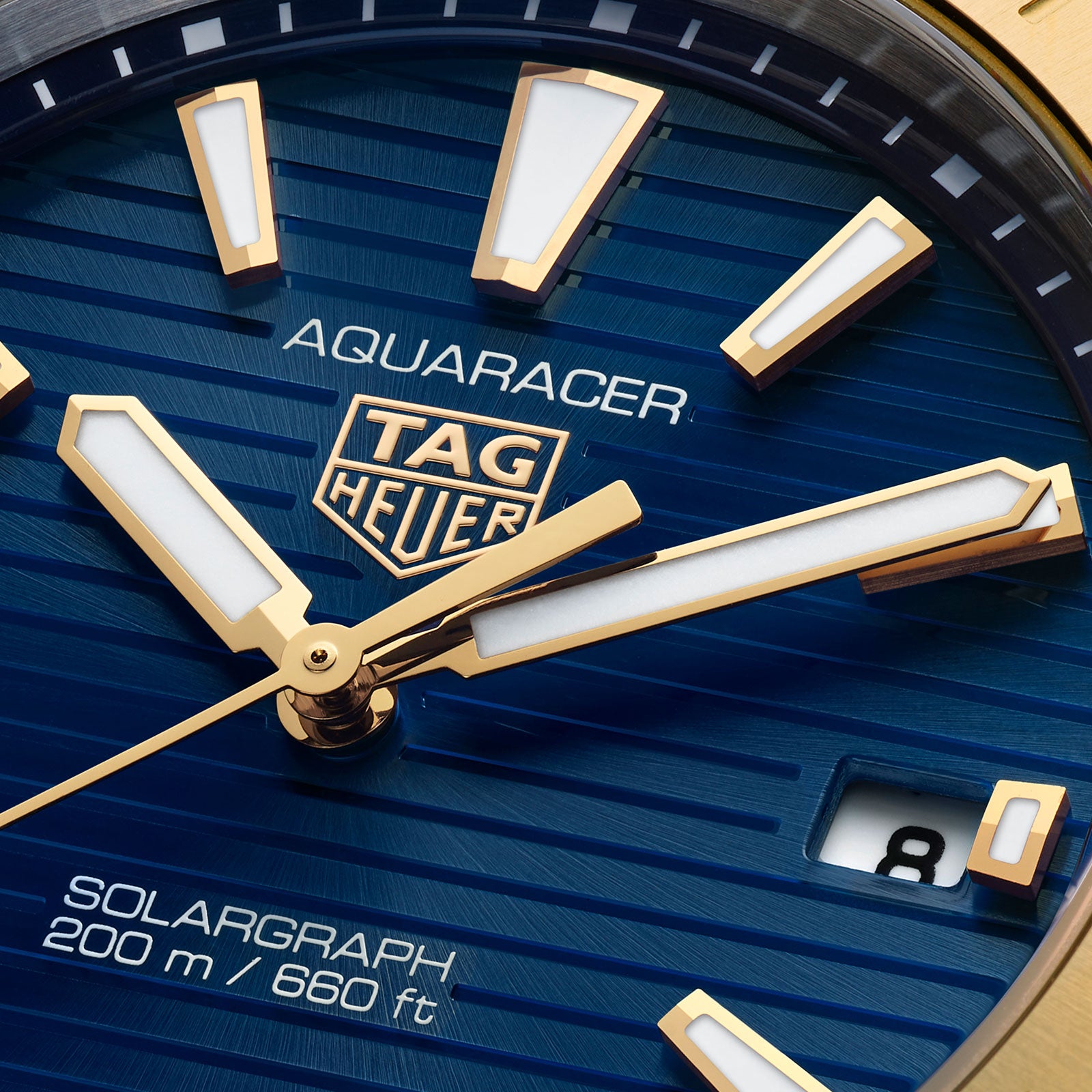 Close-up of a TAG Heuer Aquaracer Professional 200 Solargraph watch face with gold markers and hands, blue dial, date at 8, “SOLARGRAPH 200 m / 660 ft” text, and a sleek two-tone bracelet.