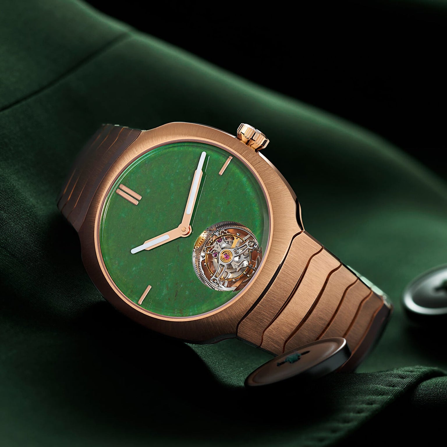 The H. Moser & Cie Streamliner Tourbillon features a green dial, red gold case and bracelet, and an exposed double hairspring flying tourbillon, displayed on dark green fabric with button accents.