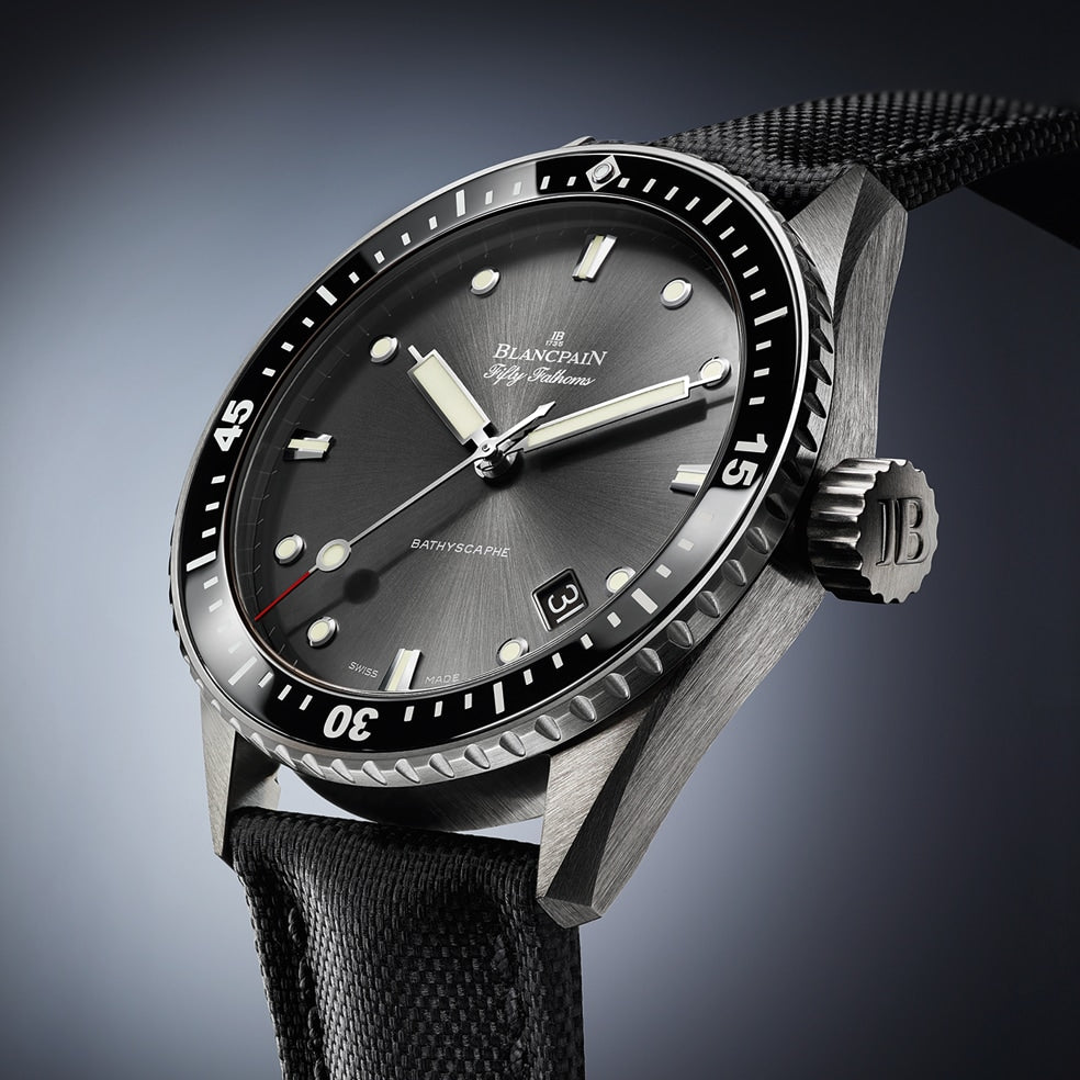 A close-up of the Blancpain Fifty Fathoms Bathyscaphe, featuring a black dial, rotating bezel, date display, and black fabric strap, powered by an automatic 1315 calibre movement.