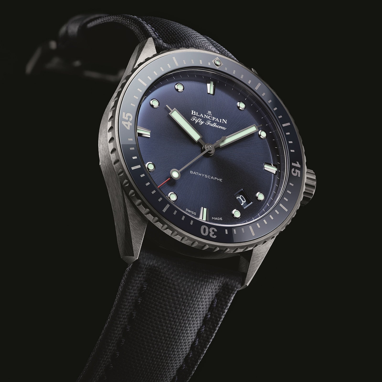 The Blancpain Fifty Fathoms Bathyscaphe features a blue dial, luminous markers, automatic movement, and a black fabric strap, shown on a black background.
