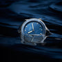 The Blancpain Fifty Fathoms Bathyscaphe, an automatic divers watch with a blue dial and rotating bezel, is partially submerged in dark water, its reflection shimmering on the surface.