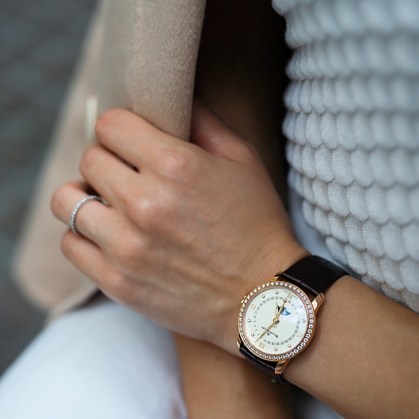 Wearing a Blancpain Villeret Quantième Phases de Lune with a diamond-encrusted case, cream dial, moon phase display, and leather strap, paired with a simple silver ring, resting on textured white fabric.