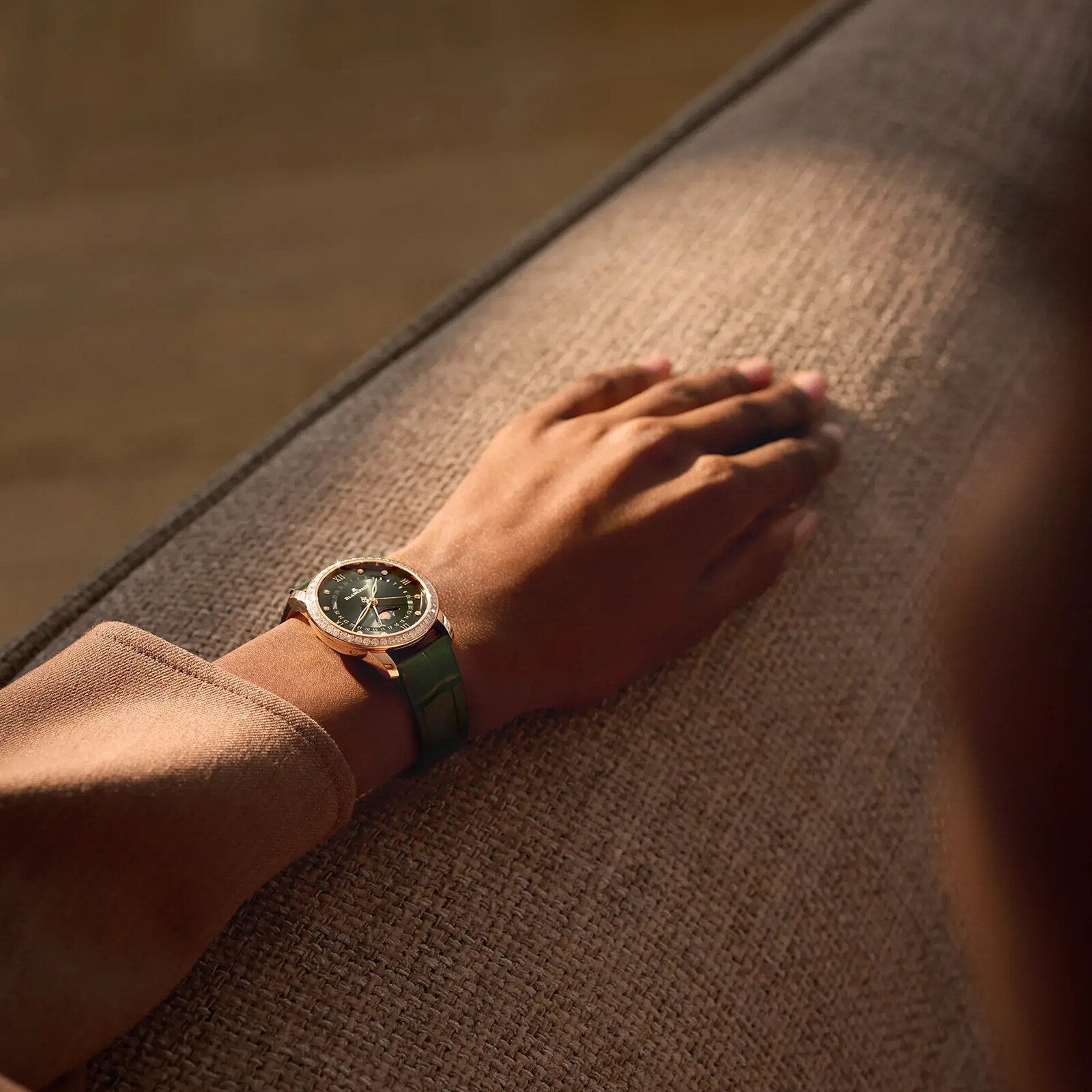 A person wearing a Blancpain Villeret Quantième Phases de Lune with a green strap rests their hand on a textured beige surface.