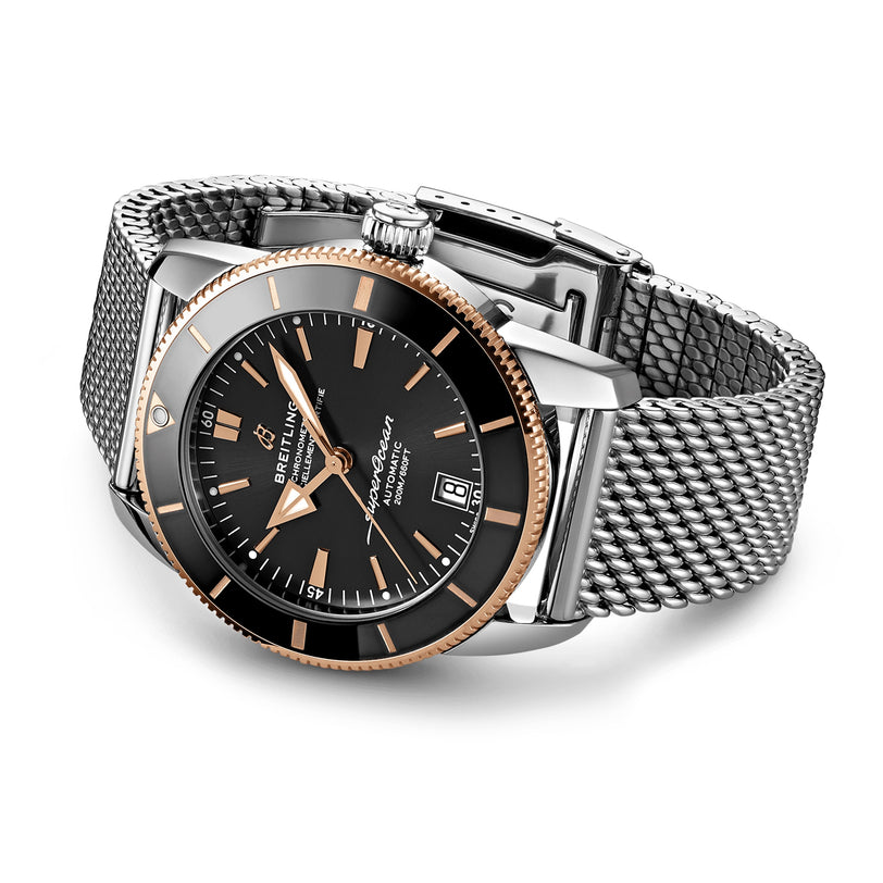 The Breitling Superocean Heritage B20 Automatic 42 features a black dial, gold bezel, metal mesh band, and date display with the precise B20 movement, displayed against a plain white background.