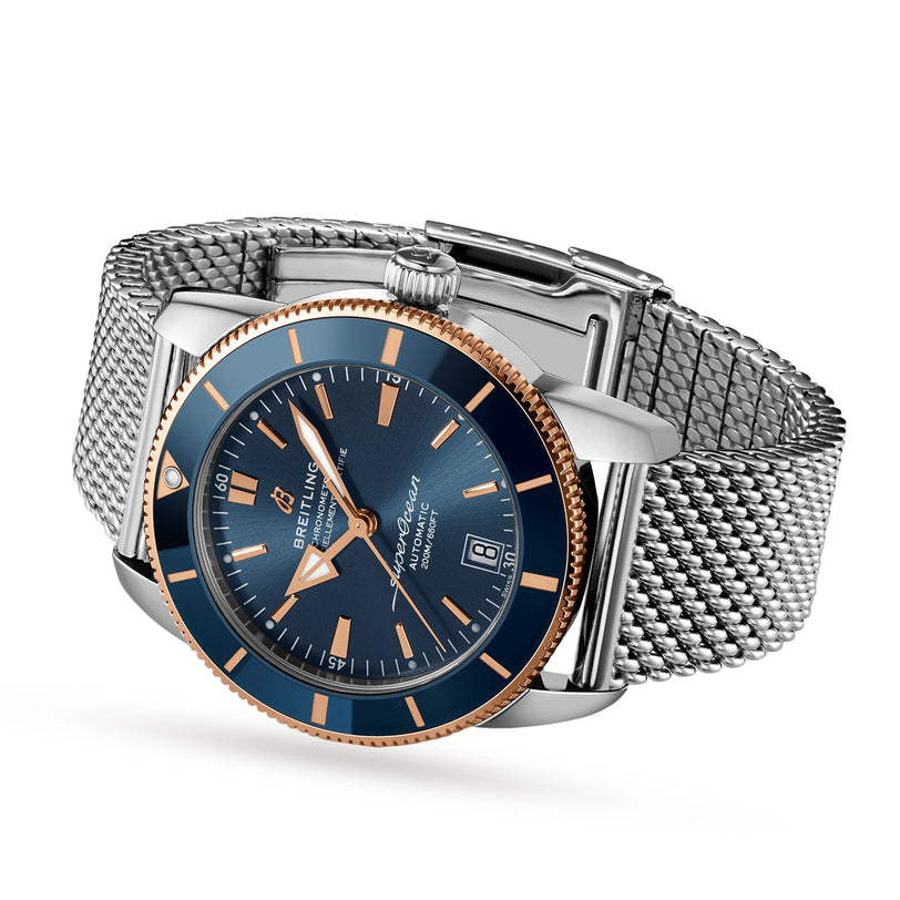 The Breitling Superocean Heritage B20 Automatic 42 wristwatch, with a blue dial, gold bezel, silver mesh band, and luminescent hands, is shown on a white background displaying the time 10:10 and date as the 8th.