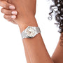 A person with curly hair wears a Breitling Chronomat 32 wristwatch with a silver Rouleaux bracelet, white dial, and Roman numerals, displaying it against a plain white background.