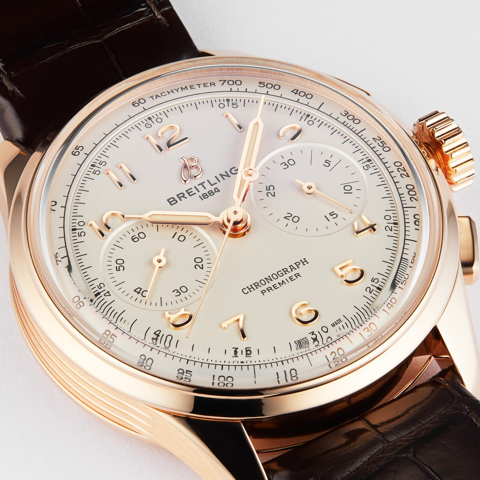 The Breitling Premier B09 Chronograph 40 features a gold case, a brown leather strap, and a white dial with multiple subdials.