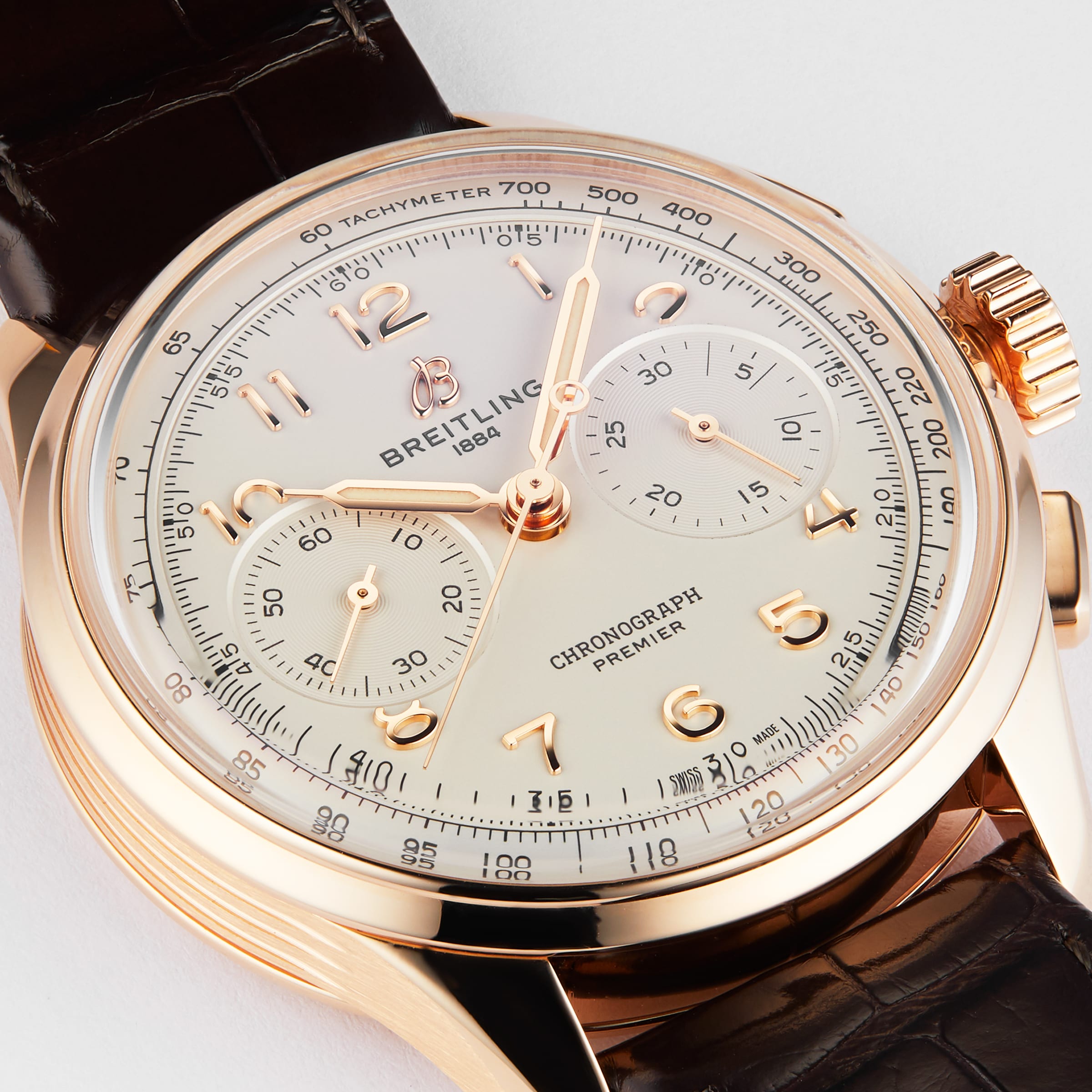 The Breitling Premier B09 Chronograph 40 features a gold case, a brown leather strap, and a white dial with multiple subdials.