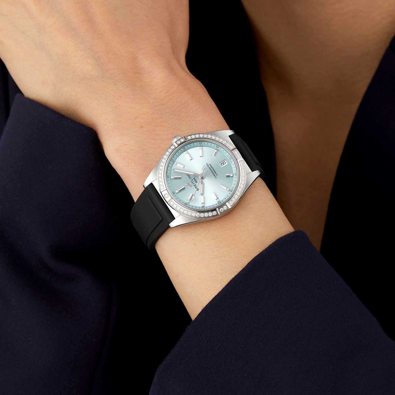 A person wearing a Breitling Chronomat Automatic 36 with a stainless steel case, light blue face, diamond bezel, date display, and black band rests their hand on their opposite arm.