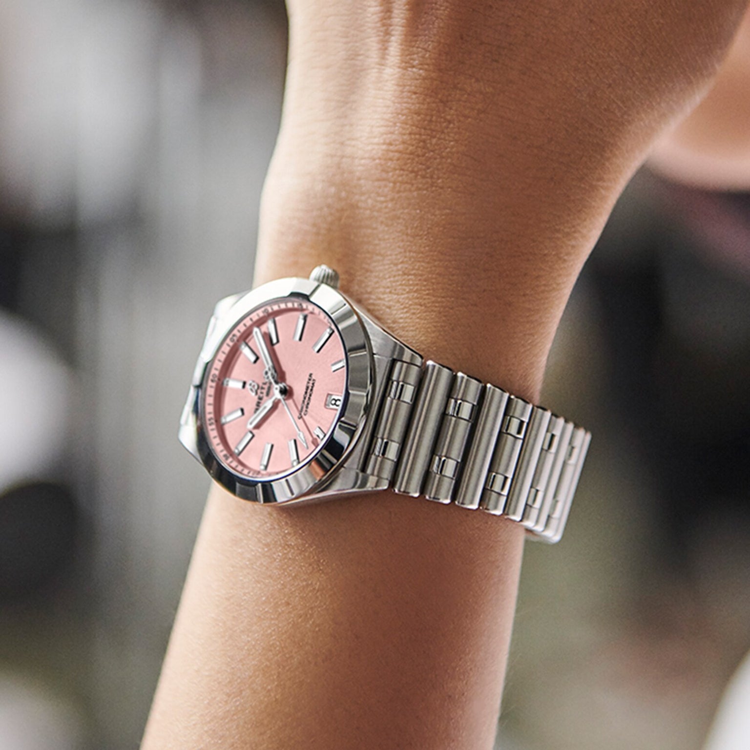 A Breitling Chronomat 32, featuring a silver Rouleaux bracelet and pink face, is worn on a persons left wrist.