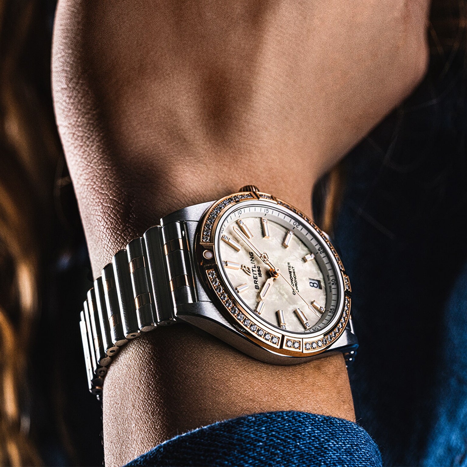 Close-up of a Breitling Chronomat Automatic 36 wristwatch in silver and gold with a diamond-set bezel and white dial, worn on the wrist. The COSC-certified timepiece shows date and time, paired with an elegant Rouleaux bracelet.