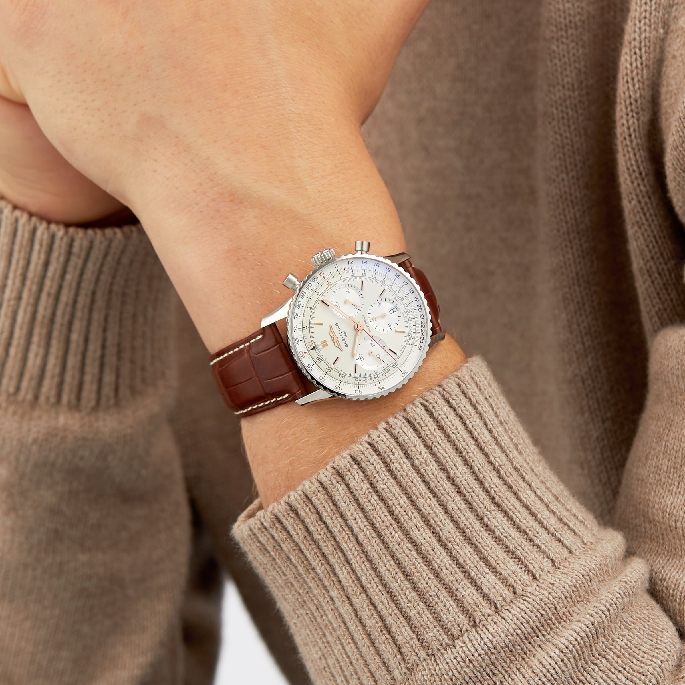 A person wearing a Breitling Navitimer B01 Chronograph 41 with a silver case, brown leather strap, and a beige sweater.