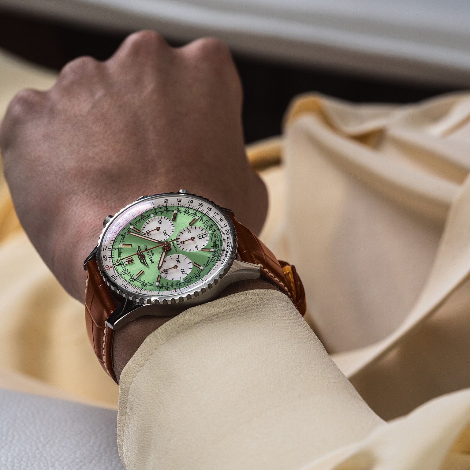 A person in a light yellow long-sleeve shirt showcases the Breitling Navitimer B01 Chronograph 41, featuring a green dial with three sub-dials and a brown leather strap.
