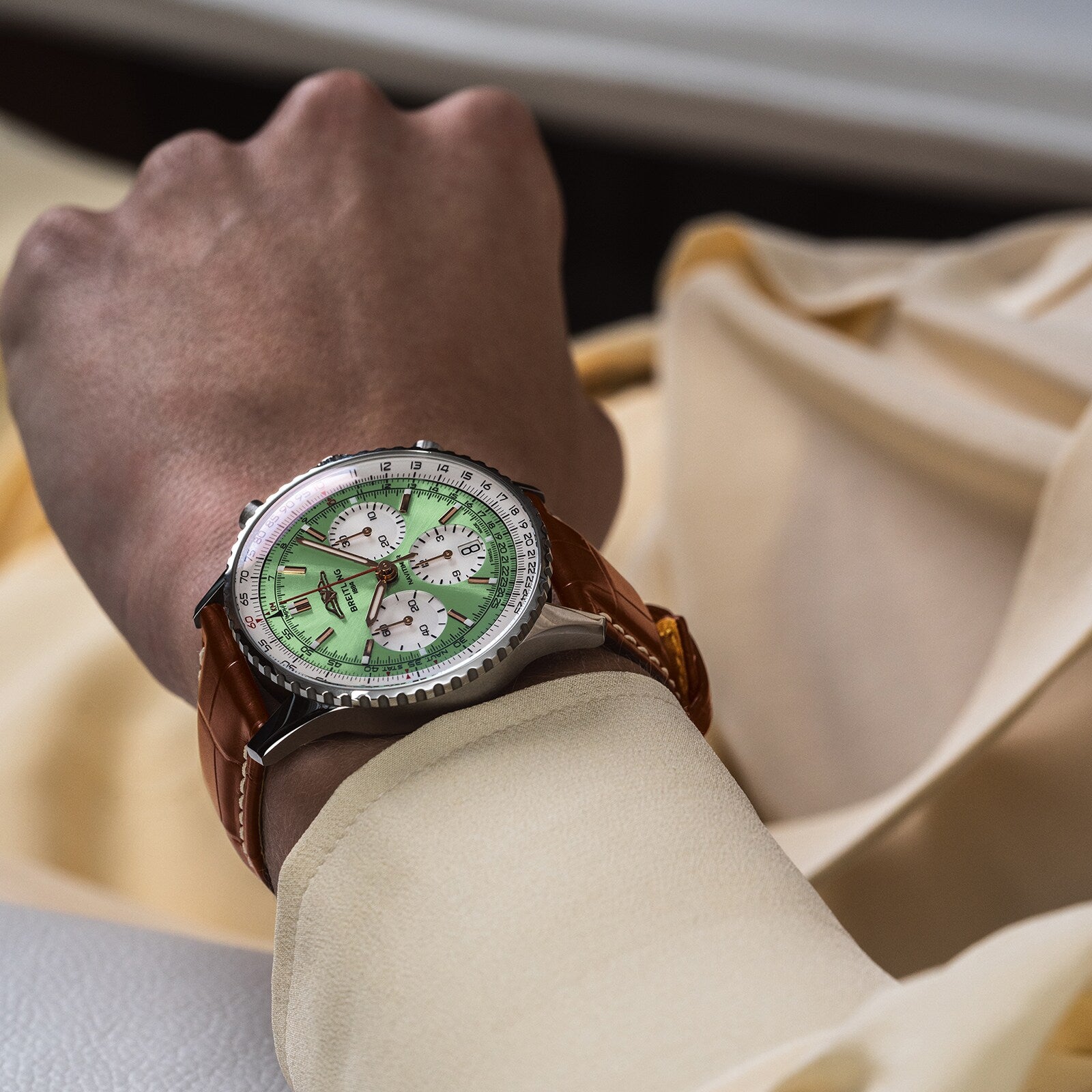 A person in a light yellow long-sleeve shirt showcases the Breitling Navitimer B01 Chronograph 41, featuring a green dial with three sub-dials and a brown leather strap.