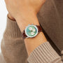 A person in a brown long-sleeve sweater showcases the Breitling Navitimer B01 Chronograph 41, featuring a green dial, white subdials, and a brown leather strap.