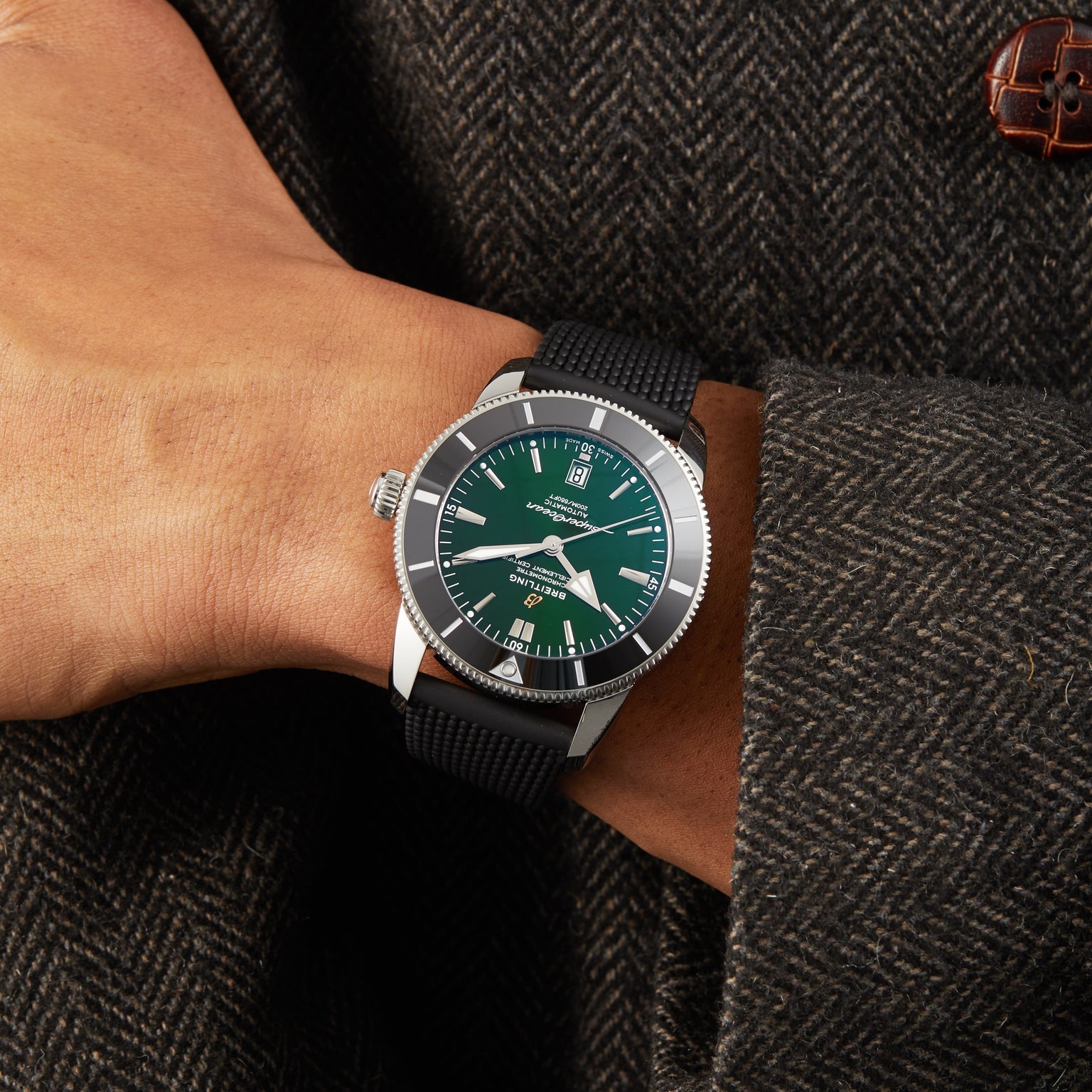 A person in a dark textured coat showcases the Breitling Superocean Heritage B20 Automatic 46 with a green dial, silver bezel, black strap, and COSC-certified Breitling B20 calibre.