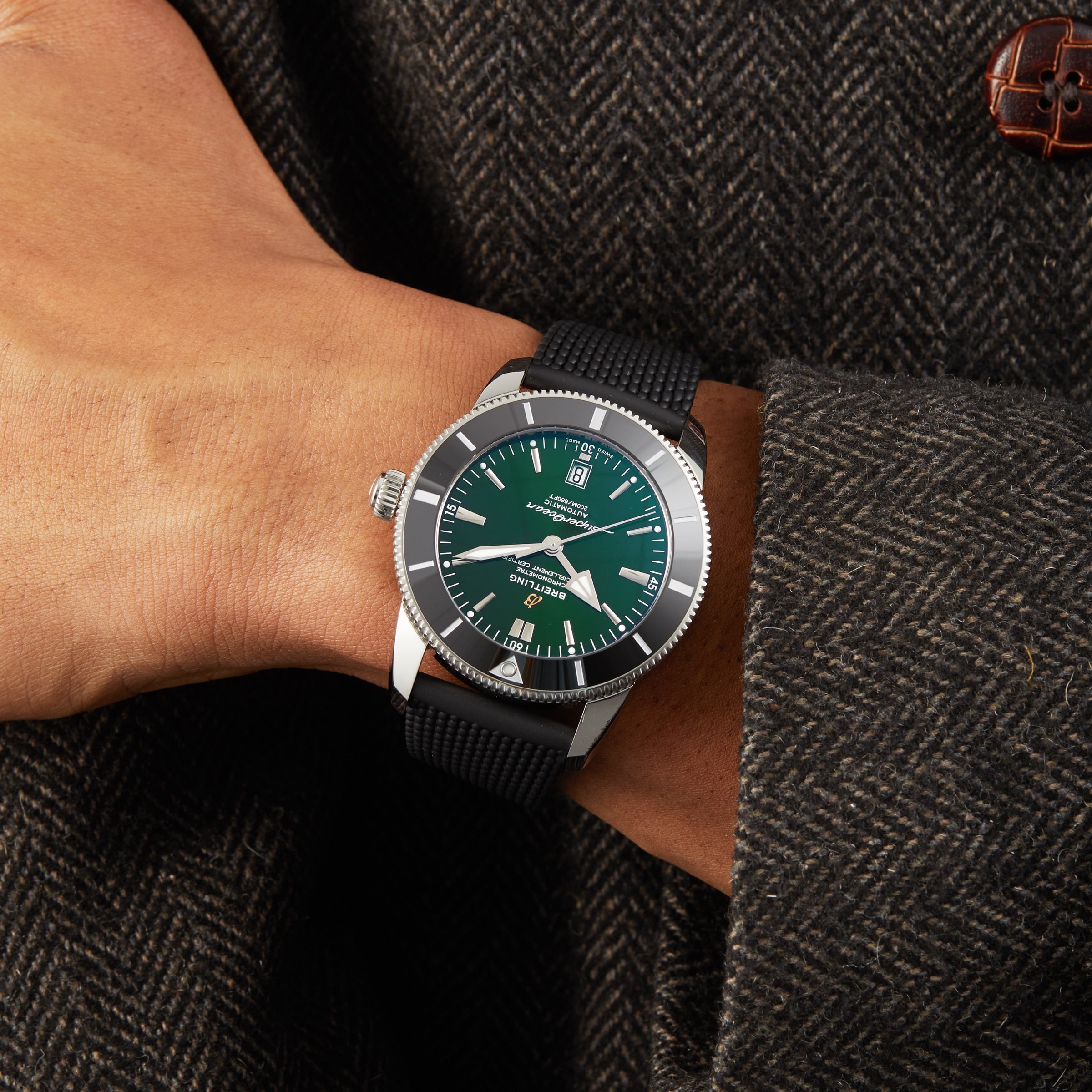 A person in a dark textured coat showcases the Breitling Superocean Heritage B20 Automatic 46 with a green dial, silver bezel, black strap, and COSC-certified Breitling B20 calibre.
