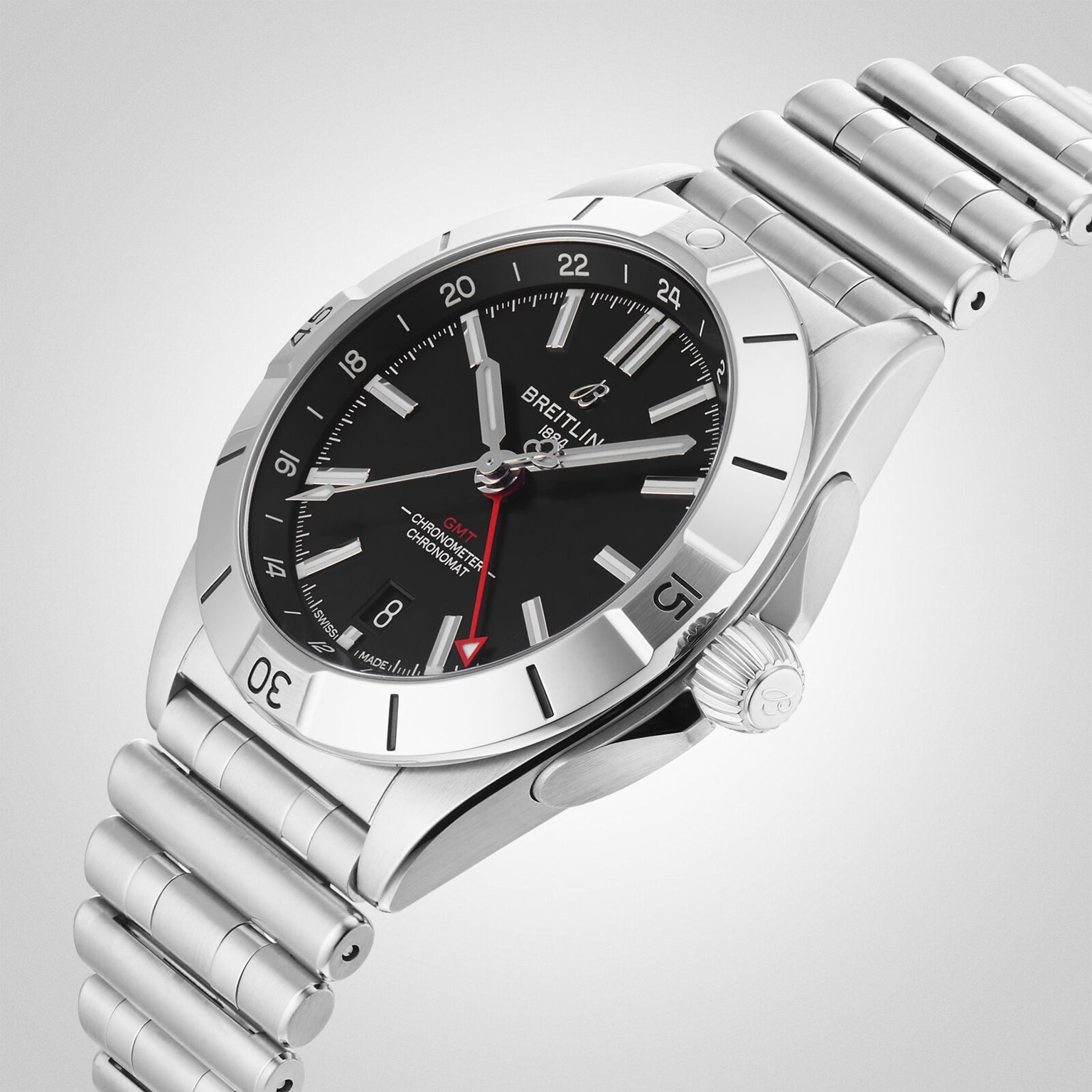 The Breitling Chronomat Automatic GMT 40 is a stainless steel wristwatch featuring a black dial, silver markers, red GMT hand, and metal link bracelet, displayed against a plain gradient background.