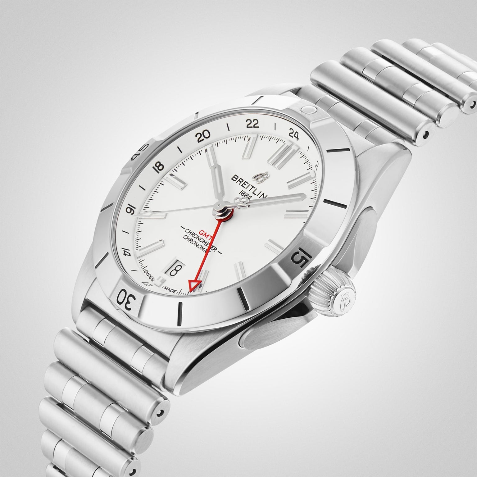 The Breitling Chronomat Automatic GMT 40 features a stainless steel case, white dial, date display, red GMT hand for dual time zones, and a metal link bracelet, set against a light gradient background.
