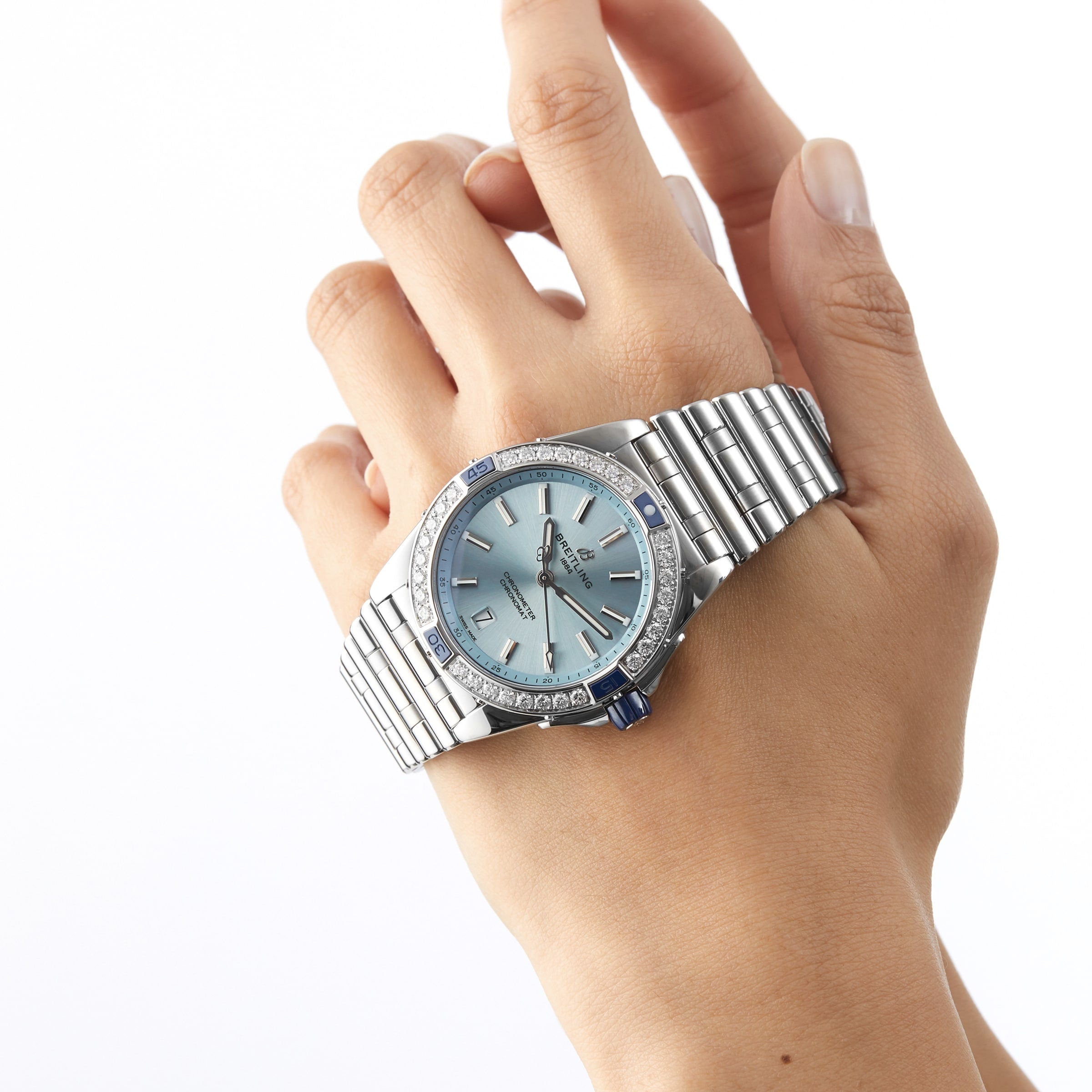 A hand wears the Breitling Super Chronomat Automatic 38, featuring a blue face and diamond accents, against a plain white background.