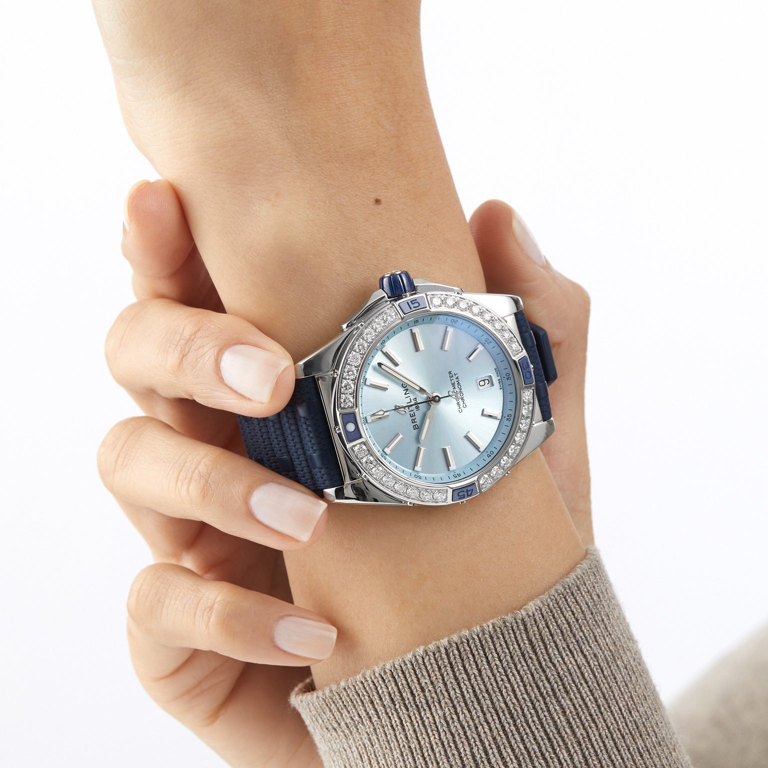 A woman's wrist in a beige sweater wears the Breitling Super Chronomat Automatic 38, the other hand touches the watch on the wrist