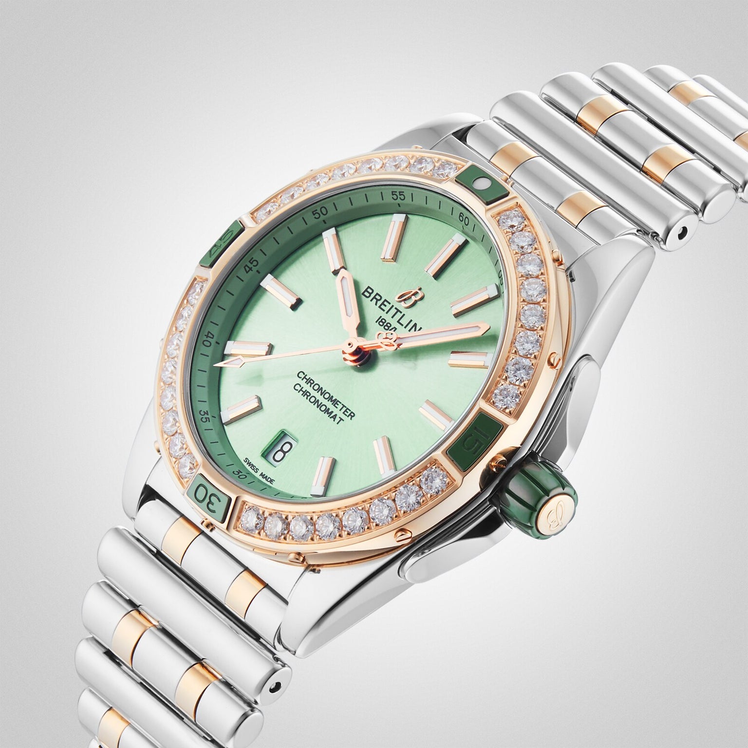 The Breitling Super Chronomat Automatic 38 wristwatch features a green dial, chronometer-certified movement, diamond-set bezel, gold accents, and a silver and gold bracelet, displayed on a light background.