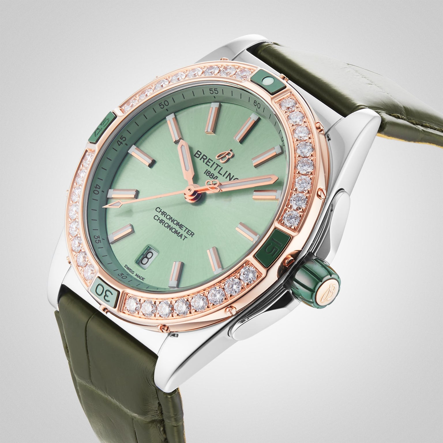The Breitling Super Chronomat Automatic 38 is a luxury mechanical watch with a green dial, diamond-set bezel, rose gold accents, and green leather strap, powered by the Breitling 17 calibre and shown at an angle on a light background.