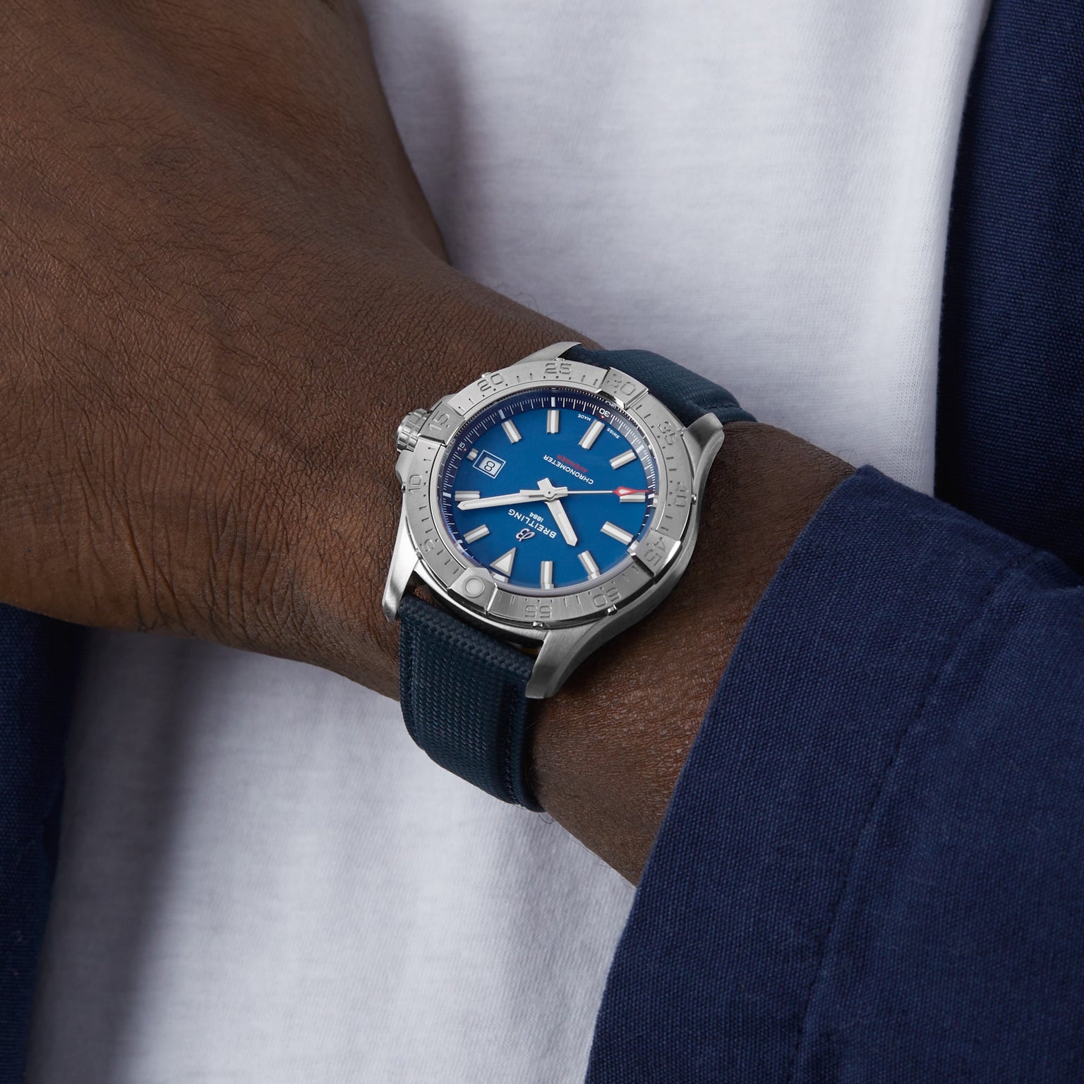 A person in a white shirt and navy jacket wears a Breitling Avenger Automatic 42, featuring a 42mm stainless steel case with a blue dial and matching blue strap.
