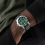 Someone wearing a Breitling Avenger Automatic 42 wristwatch in silver with a green dial and military leather strap, hand resting in their pocket.