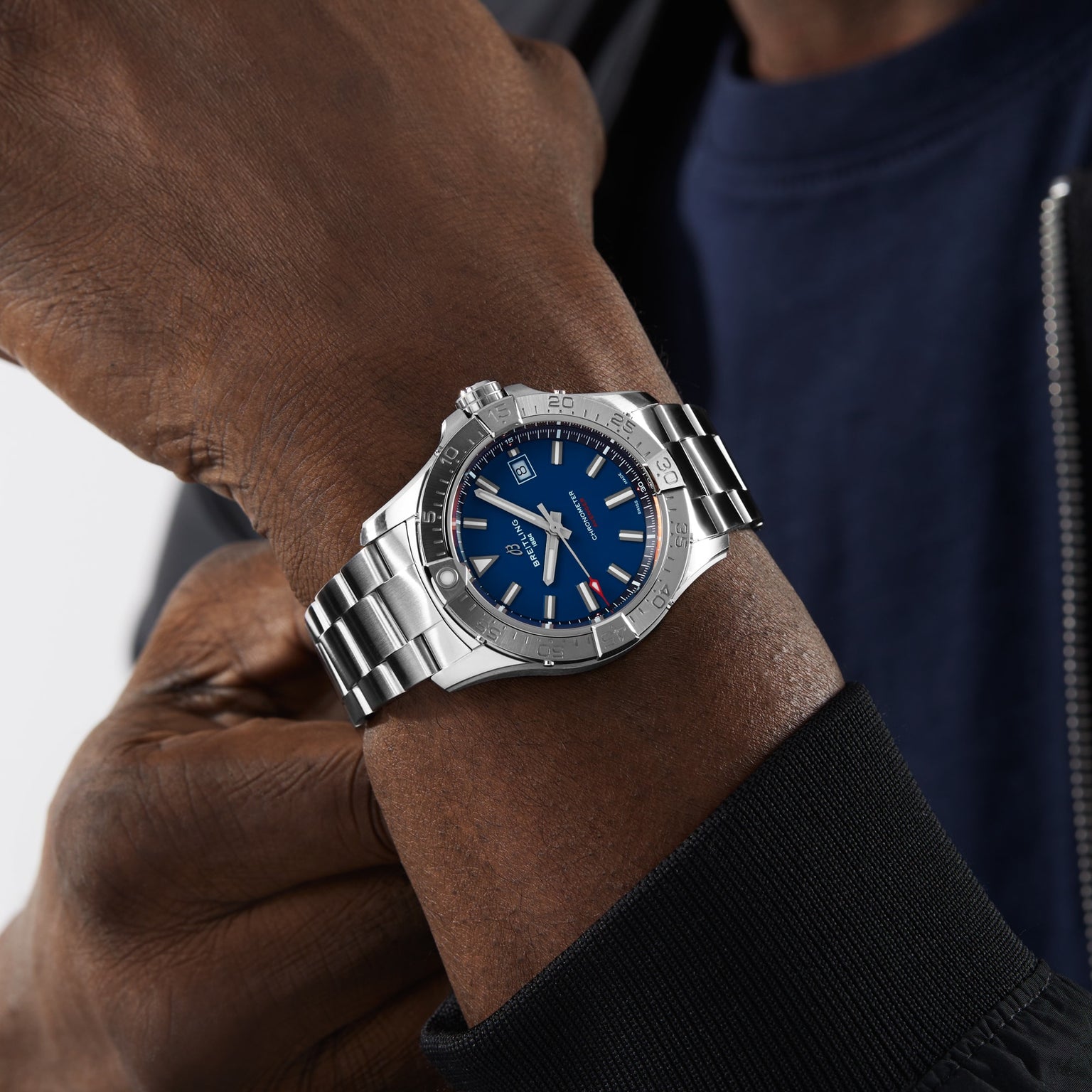 A person wearing the Breitling Avenger Automatic 42 with a blue dial, silver markers, and date window, paired with a navy shirt and dark jacket for a distinctly military-inspired style.