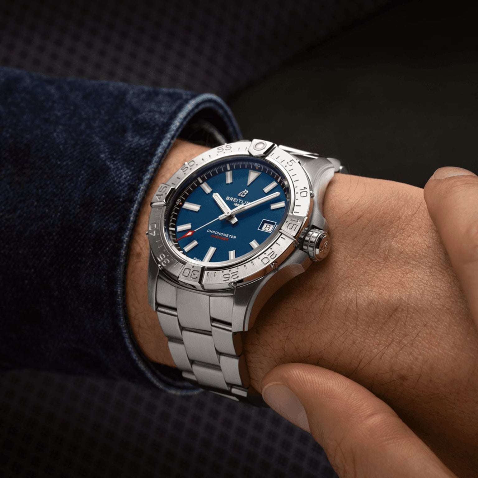 A person wears a Breitling Avenger Automatic 42 with a blue dial, silver markers, metal bracelet, and date display—its military-inspired design stands out against a dark background.