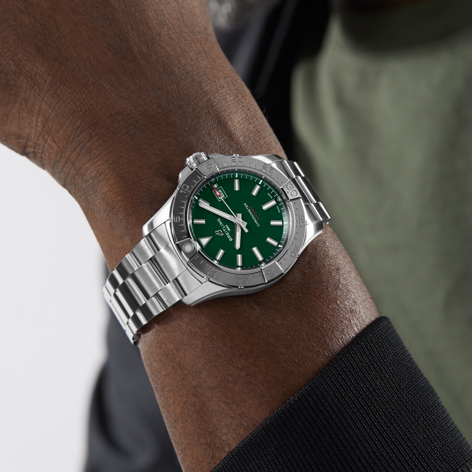 A person wearing a Breitling Avenger Automatic 42 with a military green dial and metal band on their left wrist.