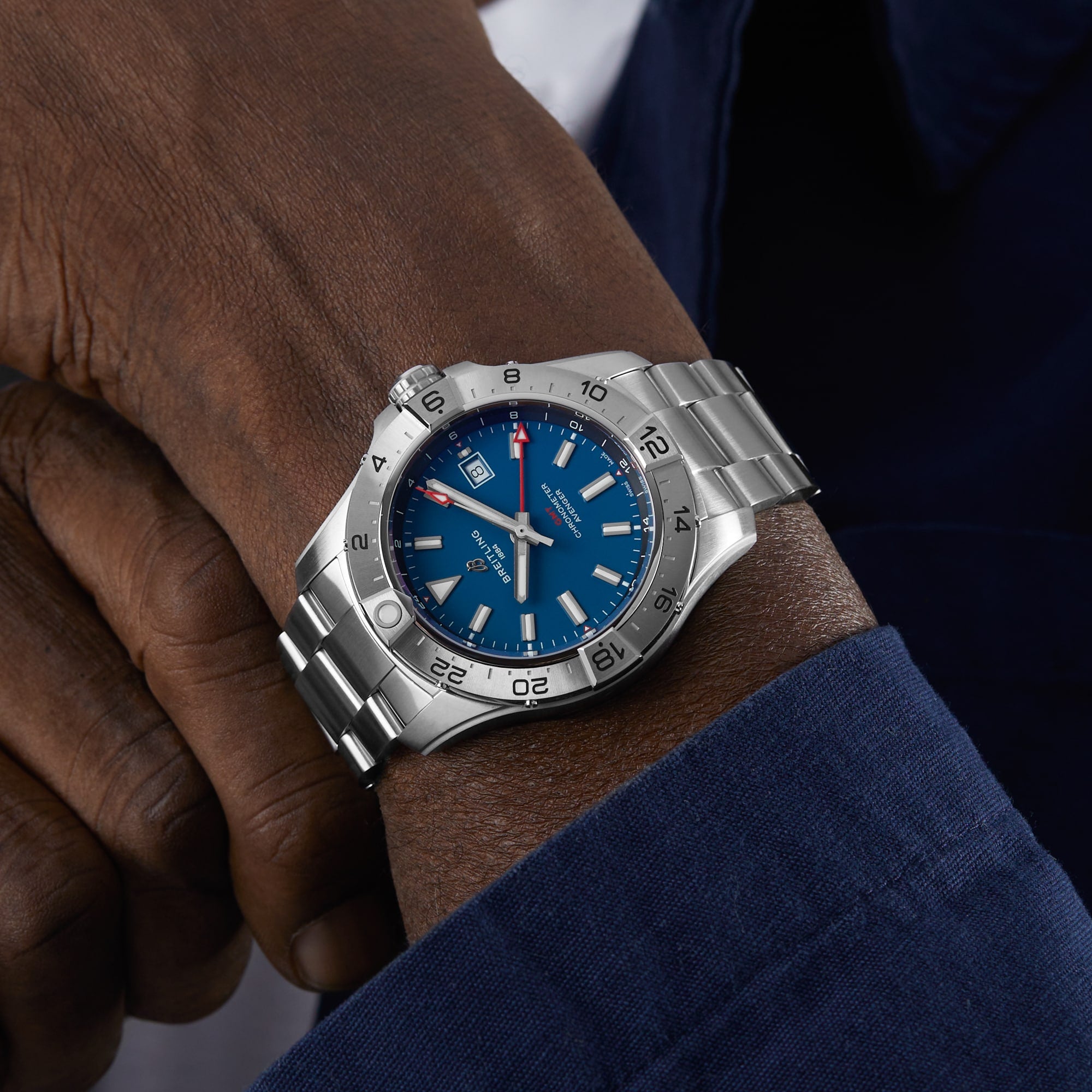A person wearing a Breitling Avenger Automatic GMT 44 wristwatch with a blue dial and stainless steel bracelet, showing the time 10:08.