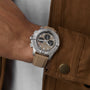 A person in a tan jacket wears a Breitling Avenger B01 Chronograph 44 with a beige strap and black subdials on their left wrist, displaying a refined military-inspired style.