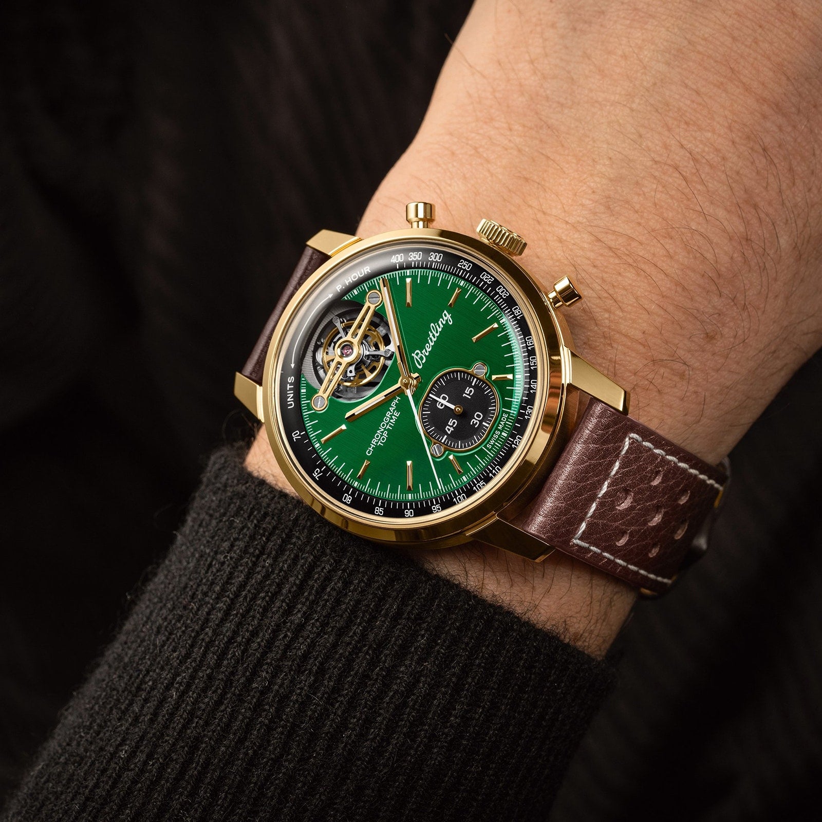 A Breitling Top Time B21 Ford Mustang gold wristwatch with a green dial, open balance wheel, vintage racing chronograph details, and a brown leather strap worn on someone’s wrist.