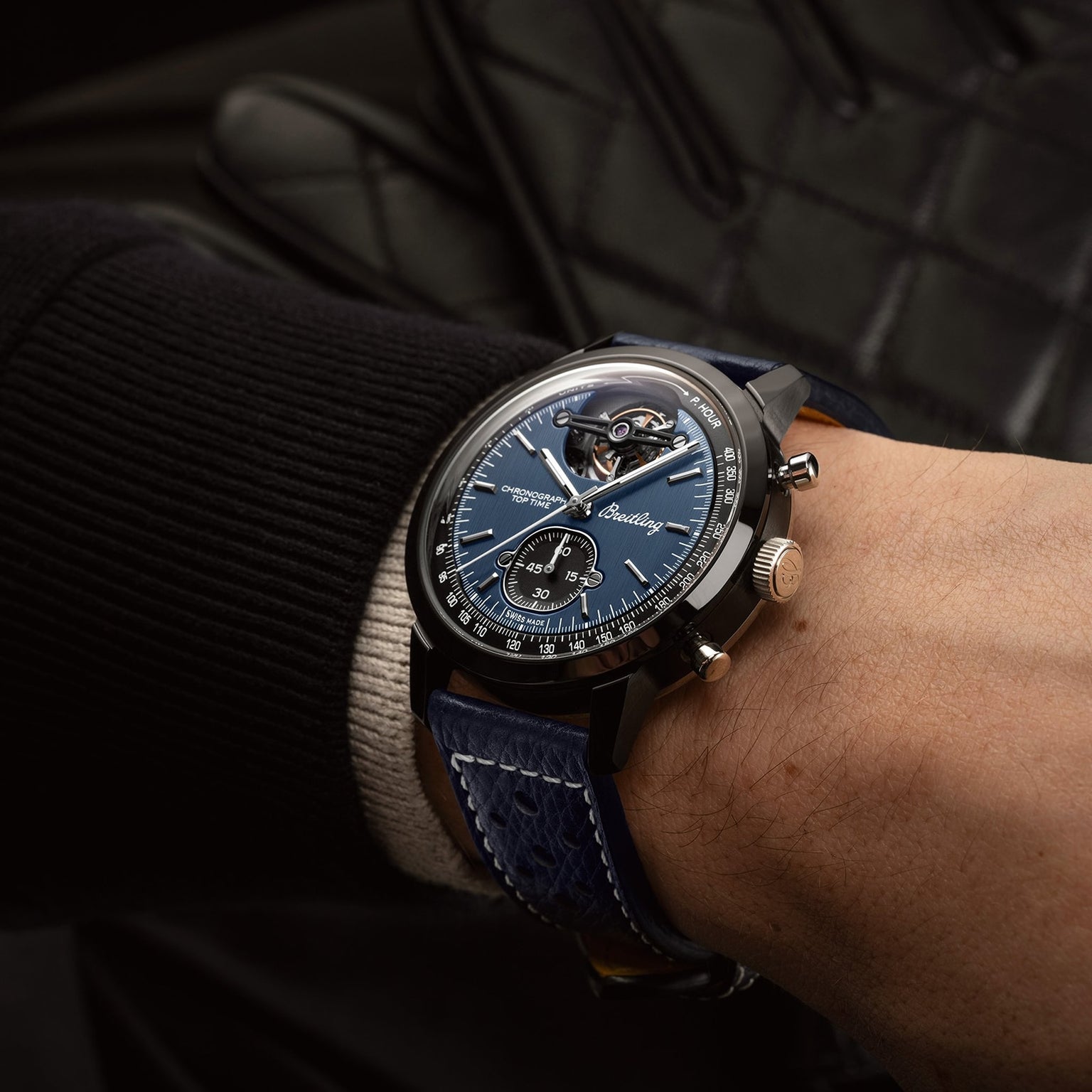 A close-up of a wrist wearing the Breitling Top Time B21 Shelby Cobra, featuring a blue dial and blue leather strap, with black clothing in the background.