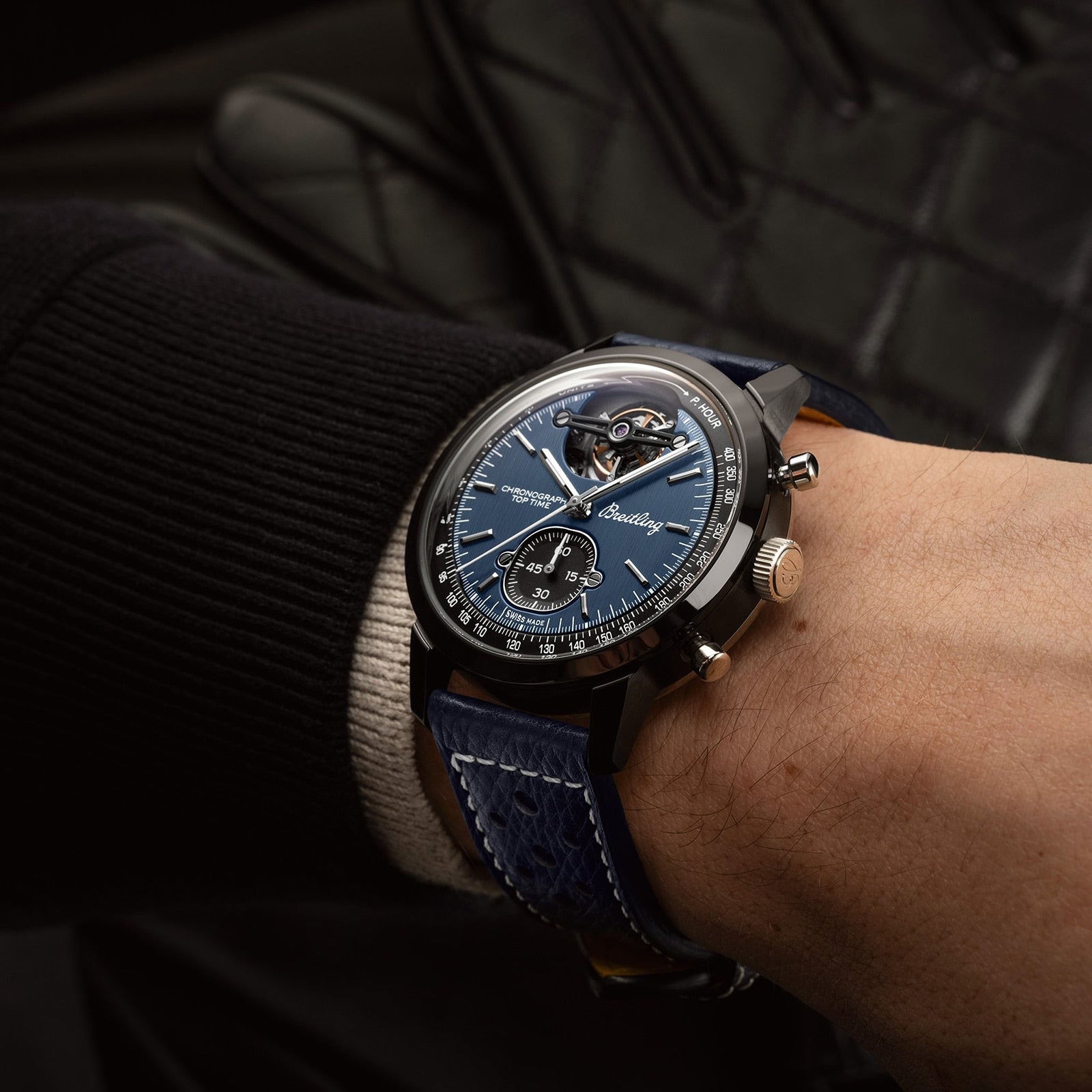 A close-up of a wrist wearing the Breitling Top Time B21 Shelby Cobra, featuring a blue dial and blue leather strap, with black clothing in the background.