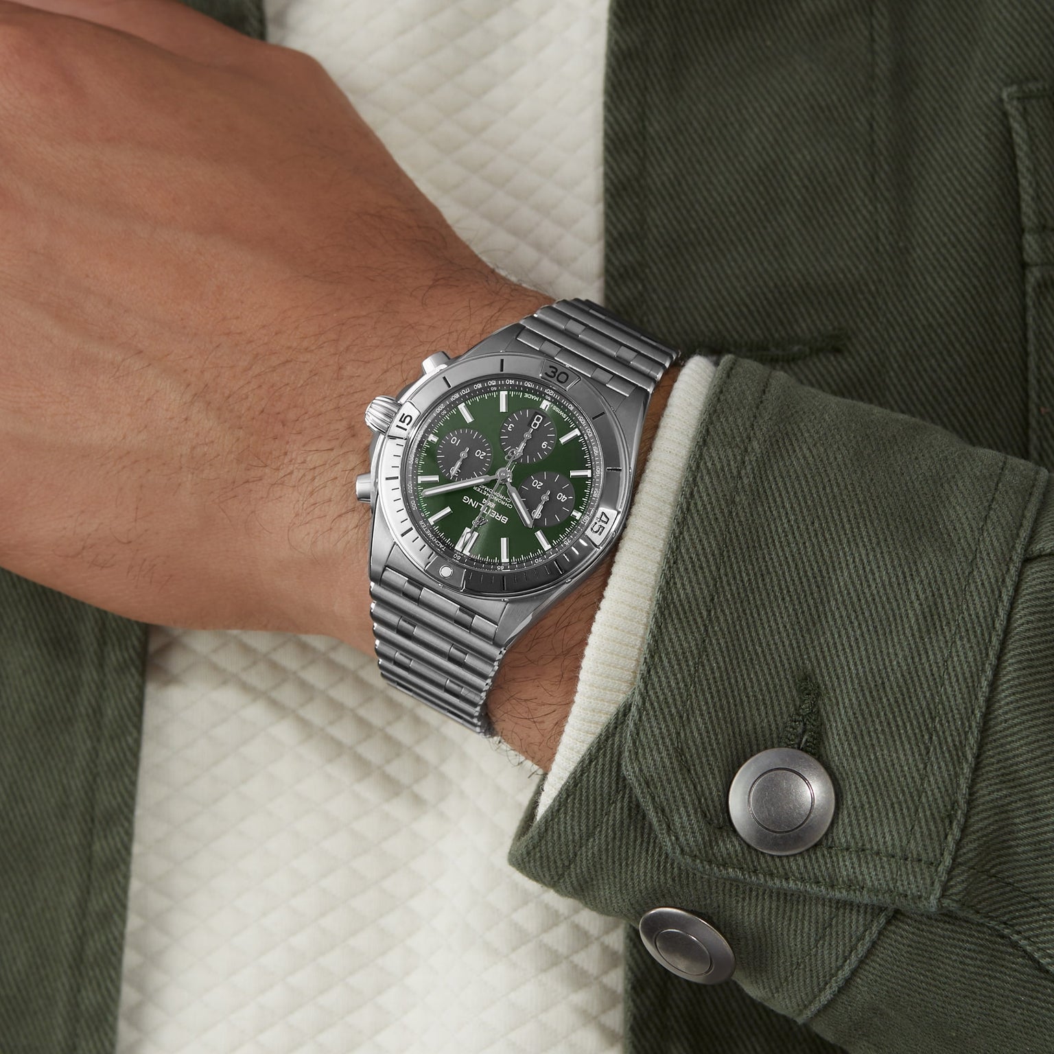 A person wearing a green jacket and a Breitling Chronomat B01 42 The Watches Of Switzerland Group Centenary Exclusive watch with a green dial on their left wrist.