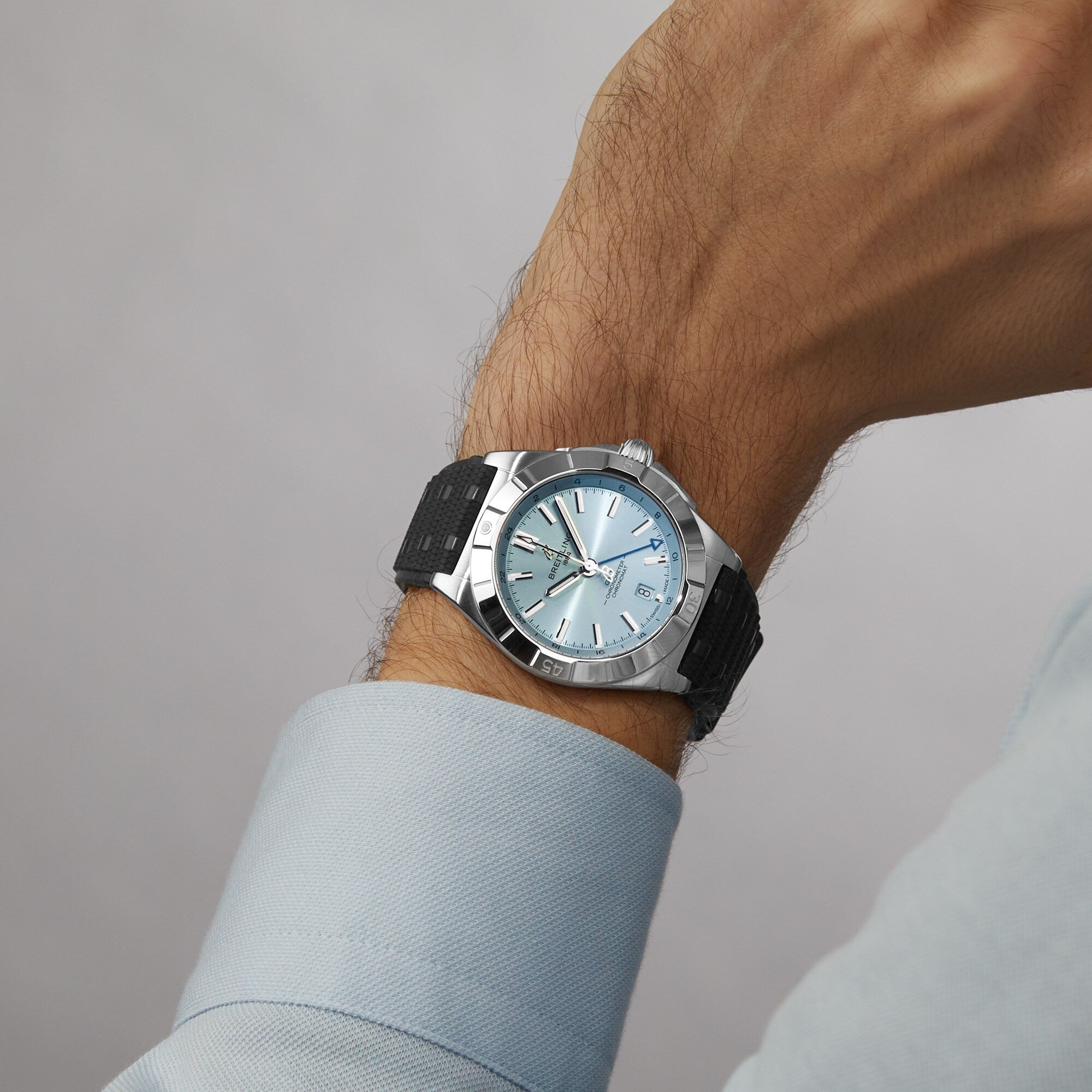 A person wearing a Breitling Chronomat Automatic GMT 40 silver wristwatch with a black band and light blue face on their left wrist.